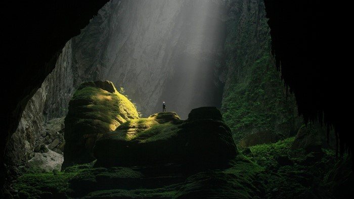 Man Standing in Sunlit Cave Amidst Mossy Rocks