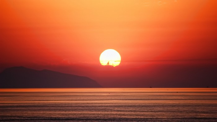 Sunset over the sea with a mountain silhouette