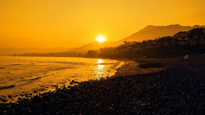 Sunset over a pebble beach with mountains and sea