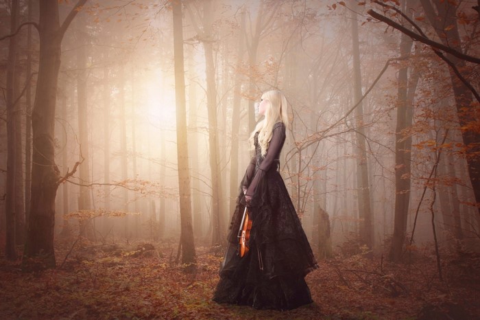 Woman in black dress holding violin in foggy autumn forest