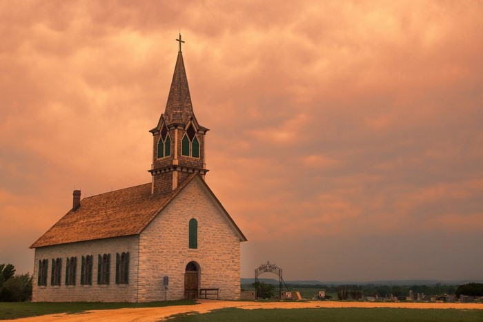 Stone church with steeple at sunset near a cemetery