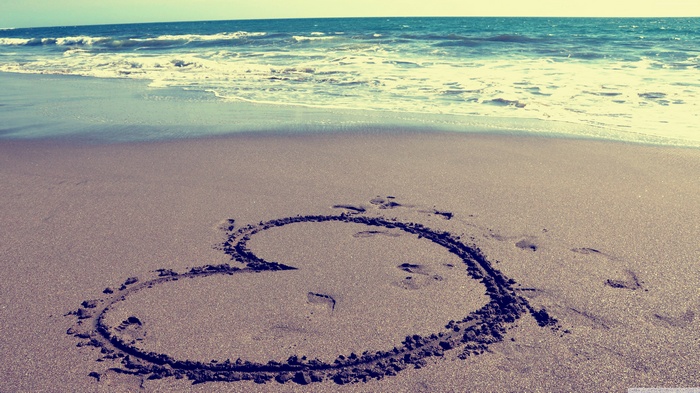 Heart drawn in sand on a beach with waves