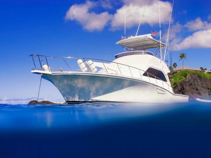 White yacht anchored in blue ocean near rocky shore