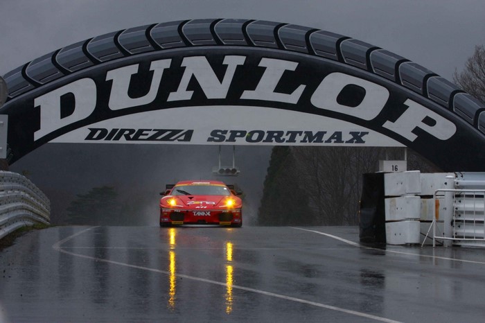 Red Ferrari race car under Dunlop arch on wet track