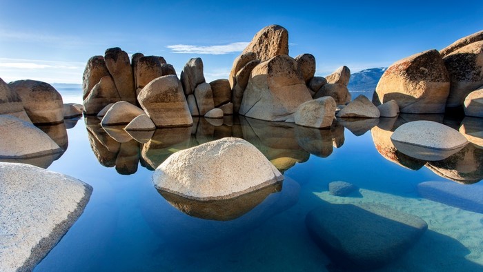 Boulders reflected in calm water under a blue sky