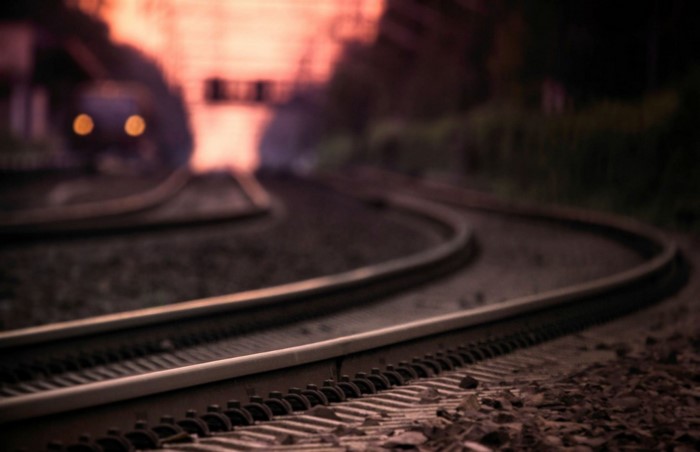 Train tracks curving at sunset with a train in the distance