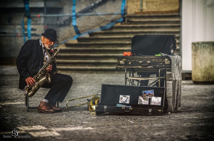 Elderly man playing saxophone on street with suitcases