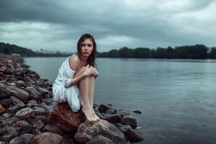 Woman Sitting on Rocks by the Sea on a Cloudy Day
