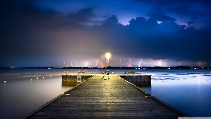 Lightning storm over a lake with a wooden pier