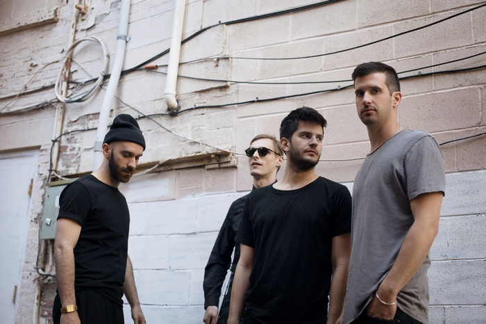 X Ambassadors band members standing against a brick wall