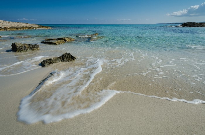 Sandy beach with rocks and clear blue ocean waves