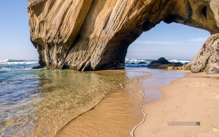 Arch rock formation on a sandy beach with ocean waves