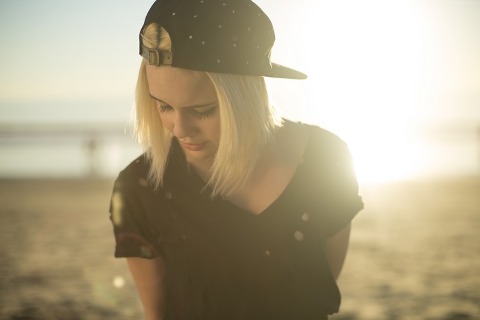 Bea Miller wearing a black cap and shirt on a beach
