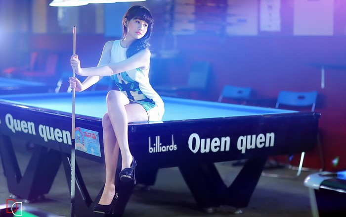 Asian woman sitting on a pool table holding a cue stick