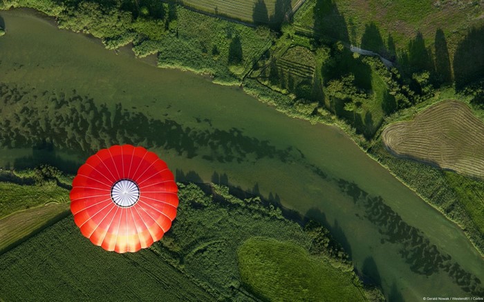 Aerial view of a red hot air balloon over a river and fields