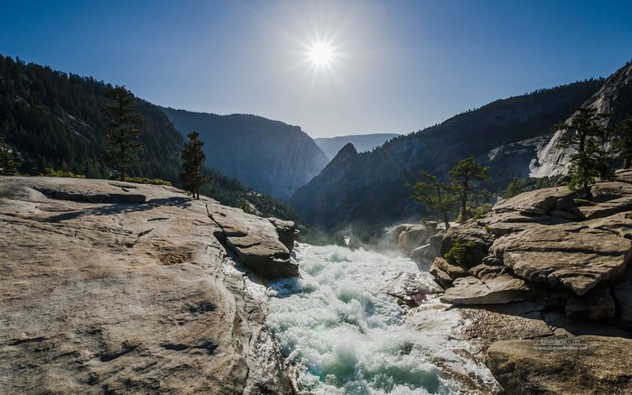 Waterfall flowing through a rocky valley under a bright sun