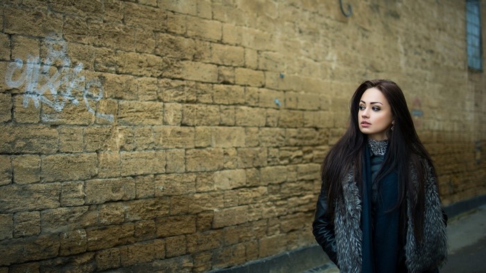Woman in fur coat standing by a brick wall