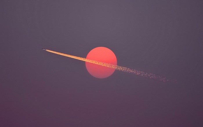 Airplane leaving contrails across a large red sun