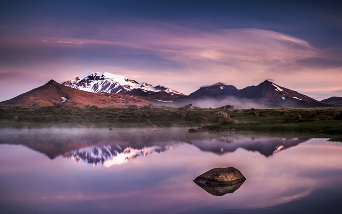 Misty mountains reflected in a calm lake at dawn