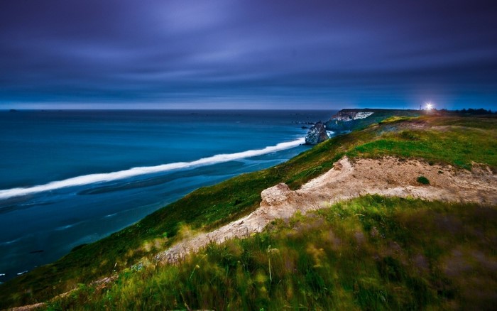 Coastal cliff overlooking the ocean at dusk with a lighthouse