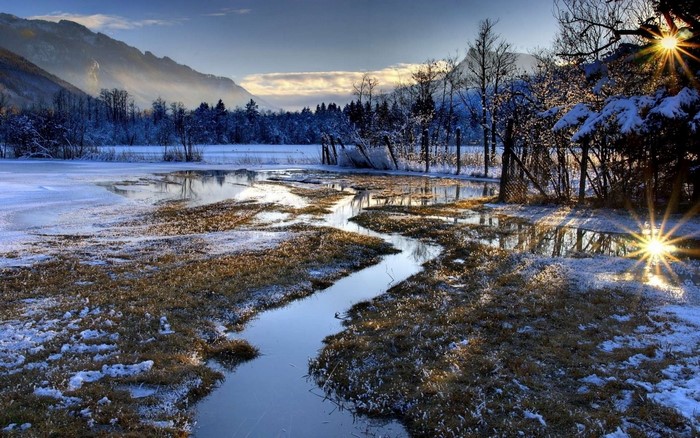 Winter landscape with frozen lake and stream at sunrise