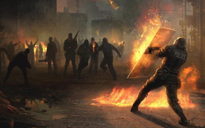 Police officer in riot gear facing a burning crowd