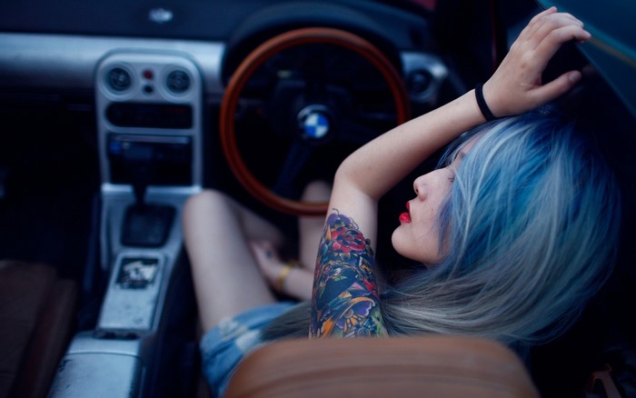Woman with blue dyed hair and tattoos in a car interior