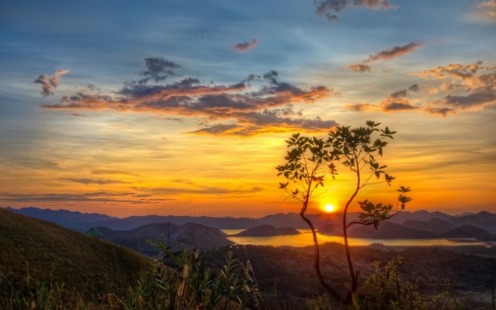 Sunset over mountains and lake with tree silhouette