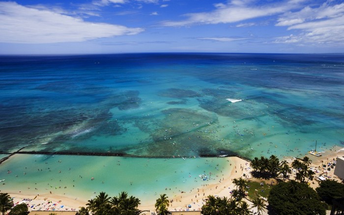 Aerial view of a crowded beach and turquoise ocean with surfers