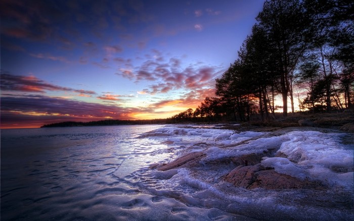 Winter sunset over a frozen lake with pine trees
