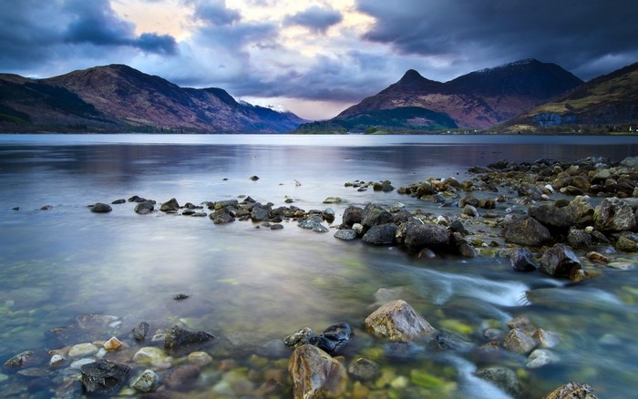 Lake with mountains and rocky shore under cloudy sky