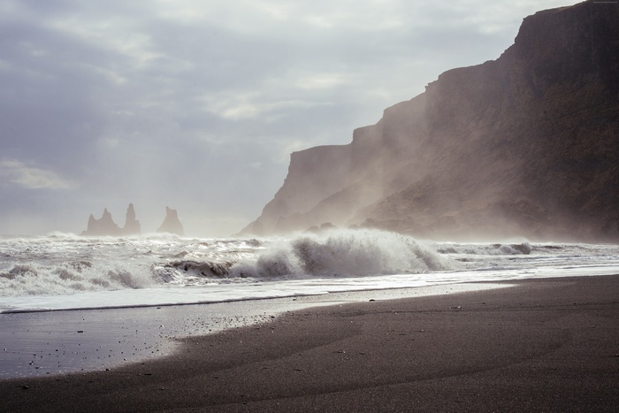 Waves crashing on a black sand beach with cliffs