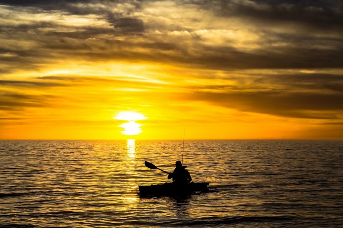 Man kayaking at sunset over the ocean