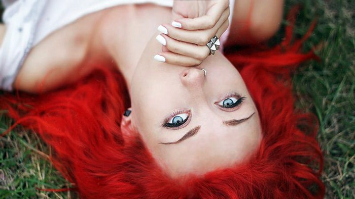 Woman with bright red hair lying on grass