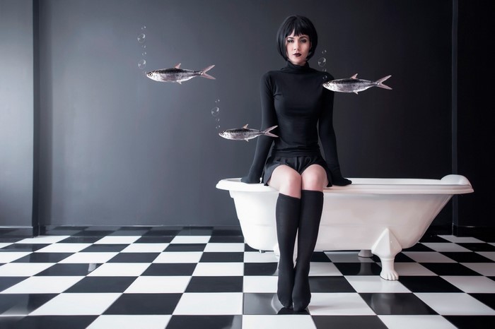 Woman in black sitting on bathtub with fish