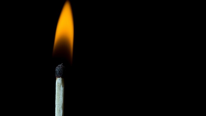 Burning match with orange flame on black background