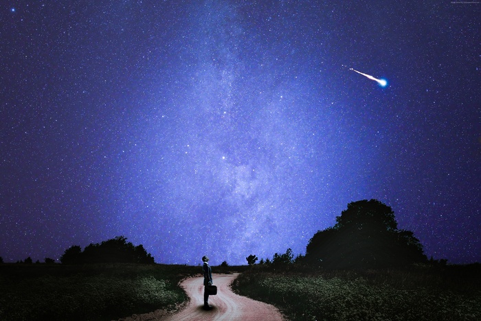 Man with suitcase looking at shooting star in night sky