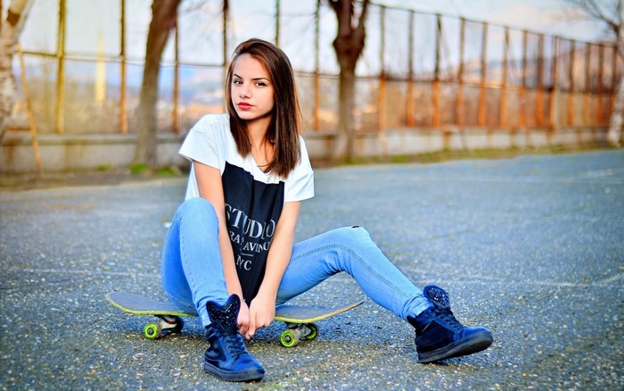 Girl sitting on a skateboard wearing jeans and sneakers