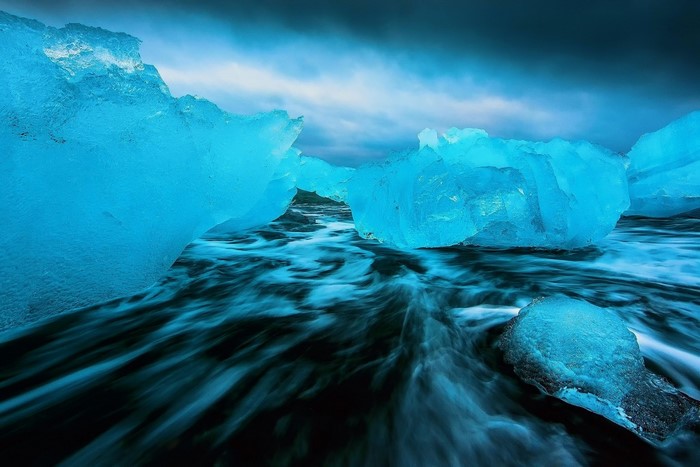 Blue icebergs on a dark, wavy sea under a cloudy sky