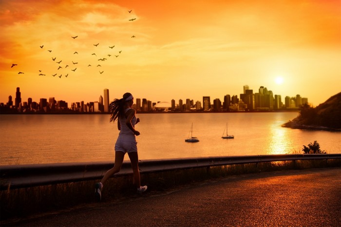 Woman running by the sea at sunset with city skyline