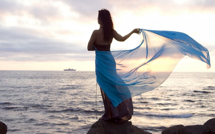 Woman in blue dress on rocks by the sea at sunset