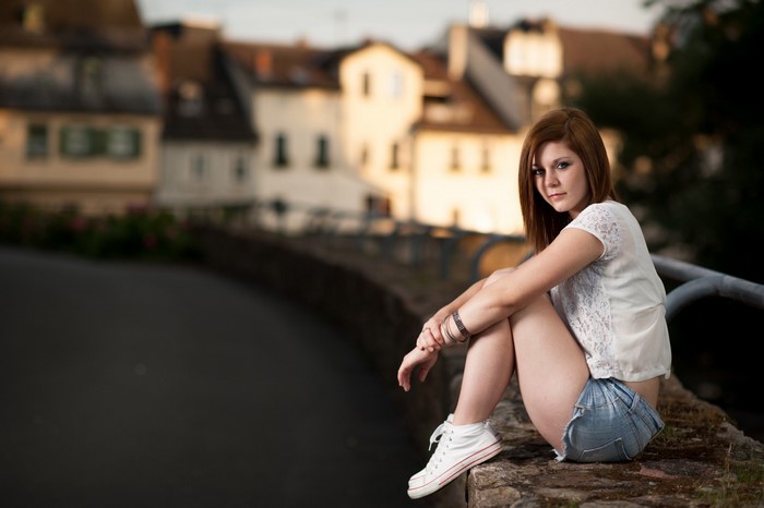 Woman sitting on a stone wall in front of buildings