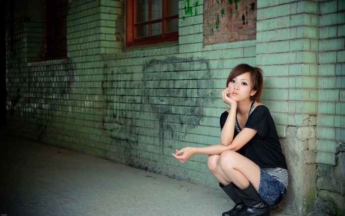 Woman squatting by a green brick wall
