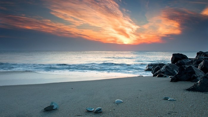 Sunset over the ocean with waves crashing on a rocky shore