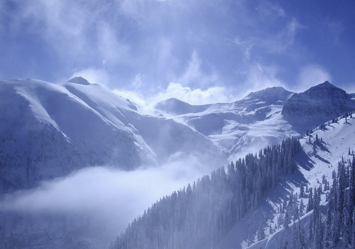 Snowy mountains with clouds and pine trees