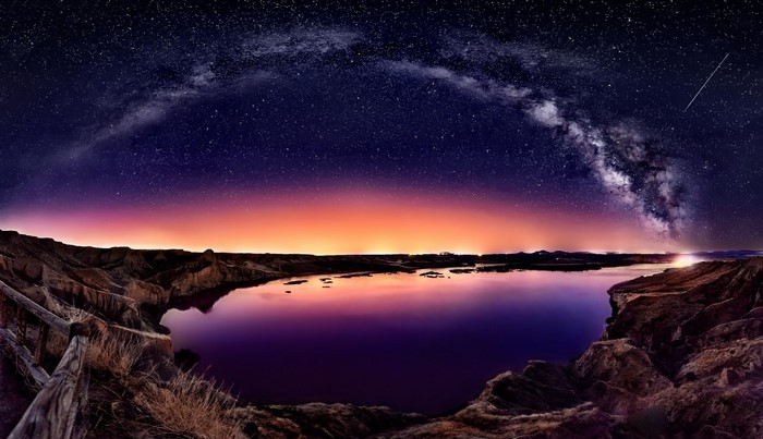 Milky Way over a lake at dusk with a fence