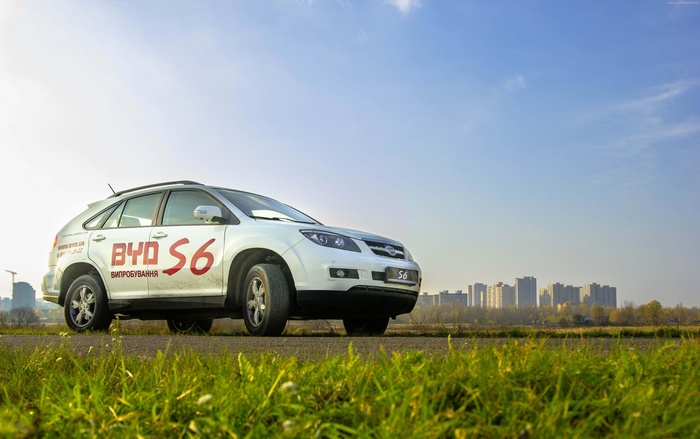 White BYD S6 hybrid car on road with city skyline