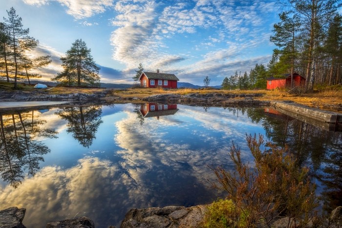Red cottages reflected in a calm lake with trees and clouds