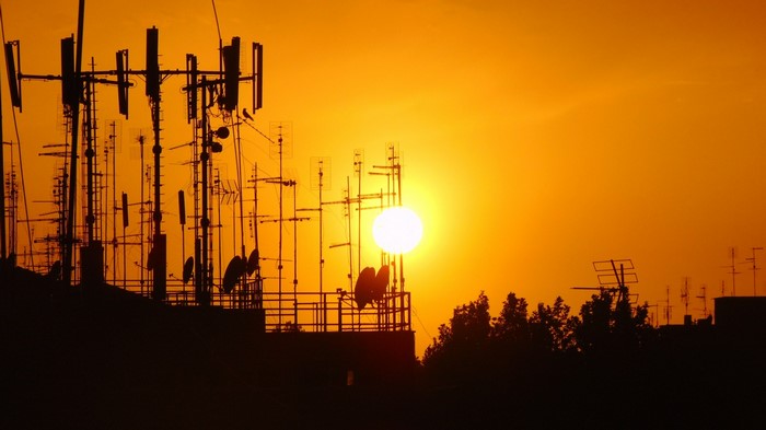 Cell towers and antennas silhouetted against a sunset