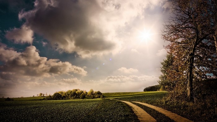 Autumn landscape with a dirt road and sunlit clouds